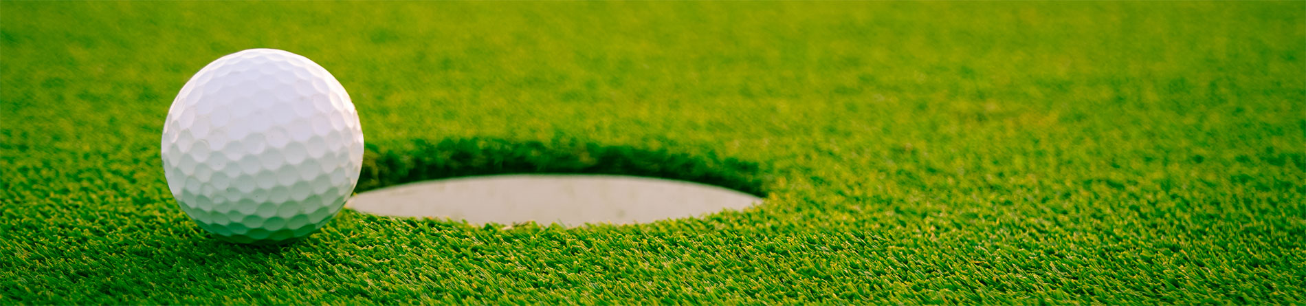 A close-up of a white golf ball resting on green grass near a golf hole on a putting green.